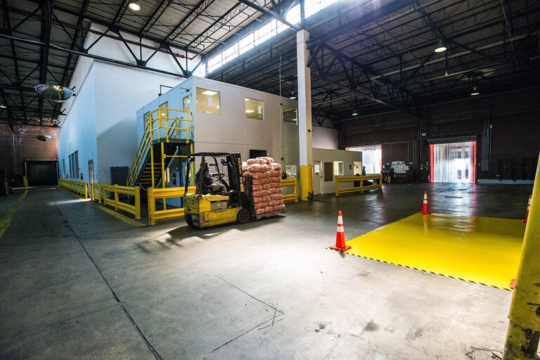 Forklift moving palletised produce through a food distribution warehouse towards refrigerated rooms with strip-curtain doors