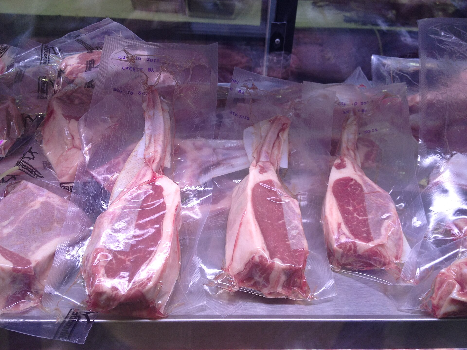 Raw bone-in beef steaks sealed in clear vacuum packaging in a refrigerated retail display