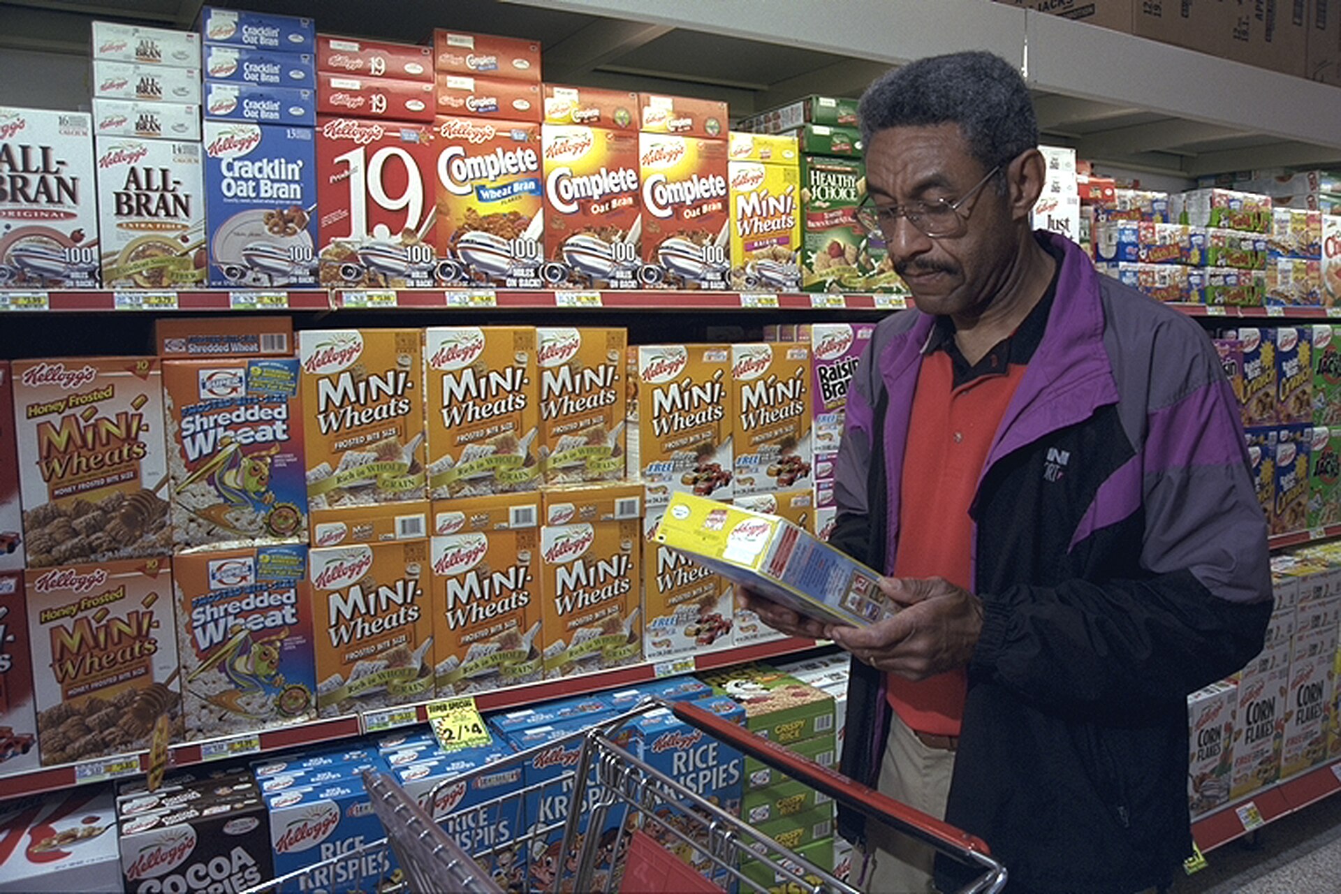 Shopper reading the ingredient panel on a boxed breakfast cereal in a supermarket aisle