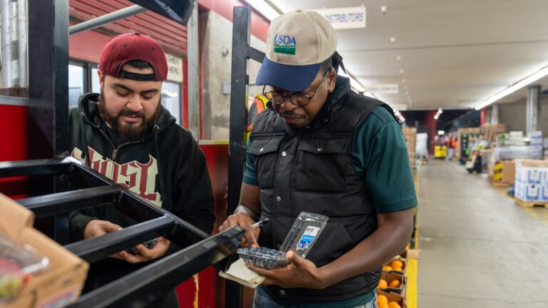 Produce market workers scanning stock among pallets at the Los Angeles Wholesale Produce Market