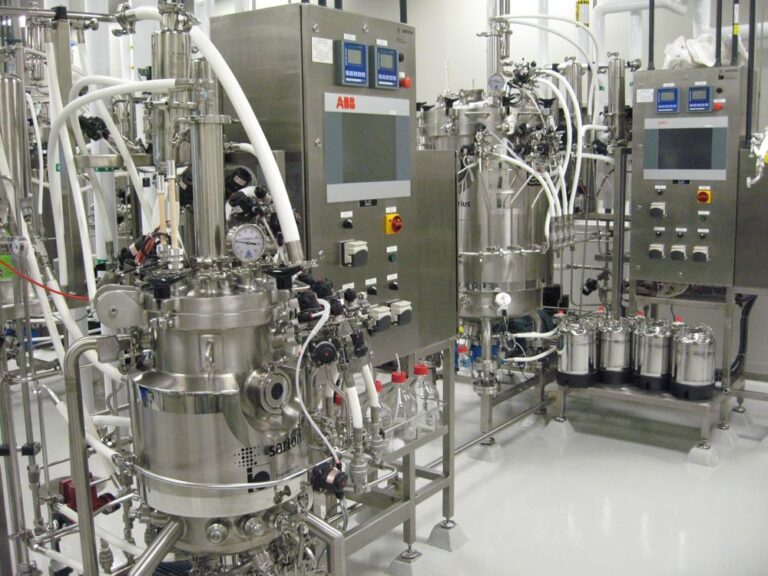 Pilot-scale stainless steel bioreactors with control panels in a bioprocessing facility