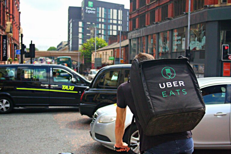 Uber Eats courier with branded delivery backpack cycling through city traffic in Manchester